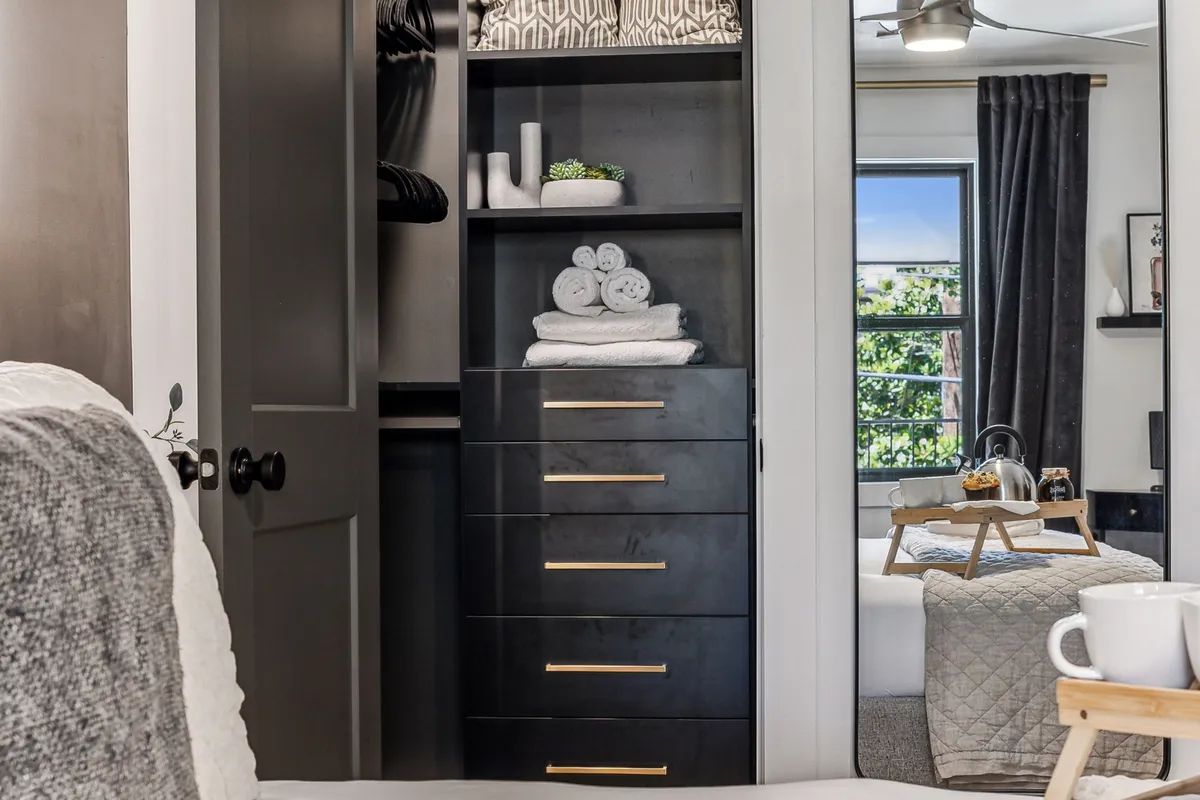 A neatly organized walk-in closet featuring smart storage solutions, soft towels, decorative touches, and a mirror. The arrangement exudes calm and order, making it easy to unpack and prepare for any event or meeting.
