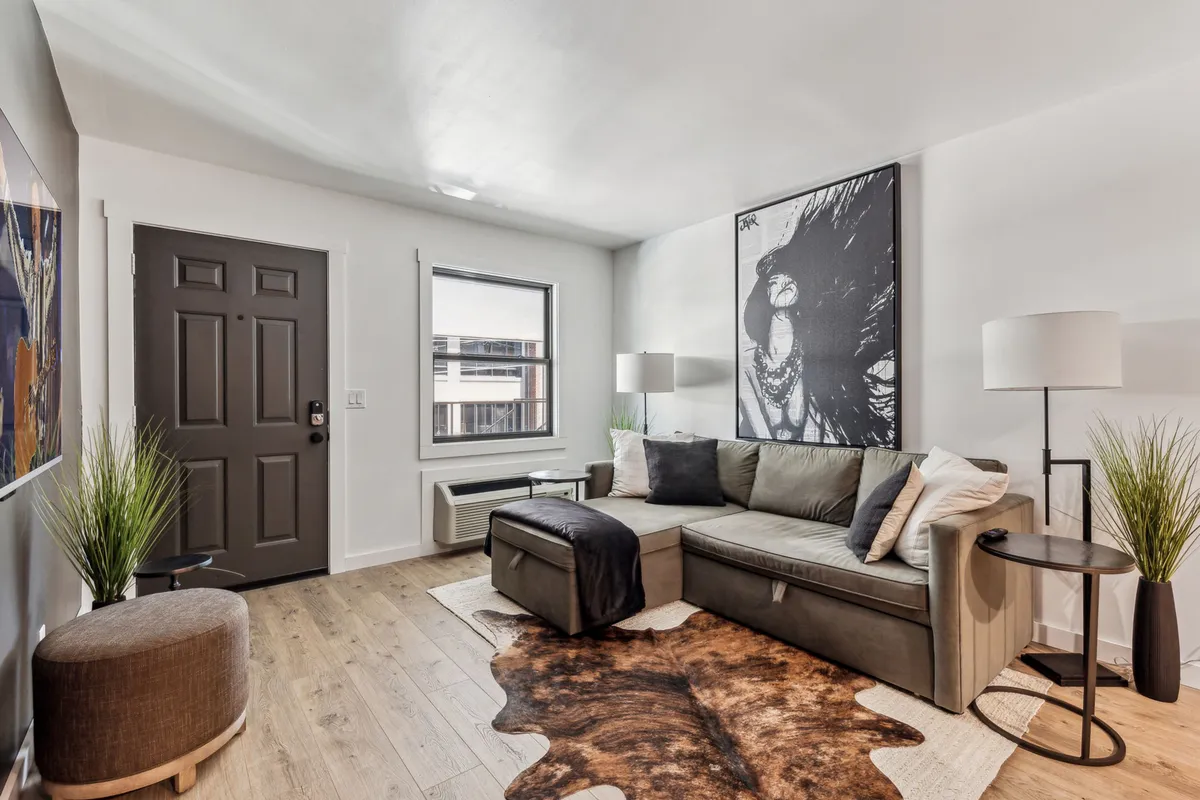 A comfortable living area centered around a soft sofa, complemented by modern artwork, a textured rug, a floor lamp, and lush plants. The design is warm and inviting, with ample space for guests to socialize or unwind after a busy day.